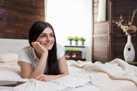 Beautiful young woman relaxing on the bed and using her tabletの写真素材