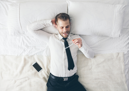 Top view. Young handsome businessman with glasses lying on the bedの写真素材