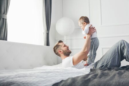 Happy father with his one year old son playing at home on the bedの写真素材