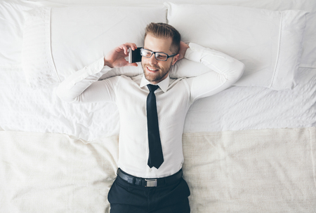 Top view. Young handsome businessman with glasses lying on the bedの写真素材