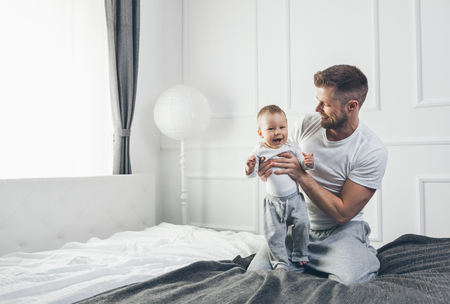 Happy father with his one year old son playing at home on the bedの写真素材
