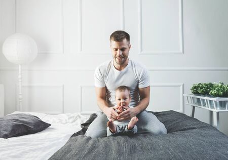 Happy father with his one year old son playing at home on the bedの写真素材
