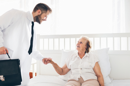 Providing care and support for elderly. Doctor visiting elderly patient at home.の写真素材