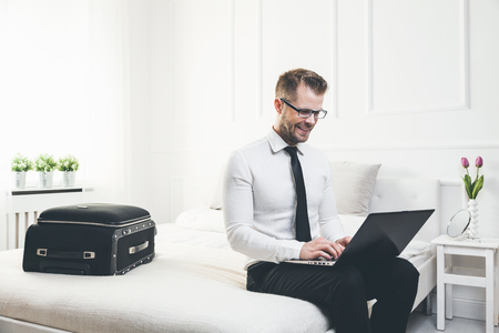Young businessman on bed working with a laptop from his hotel roomの写真素材
