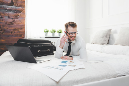 Young businessman working from a hotel room with his mobile phoneの写真素材