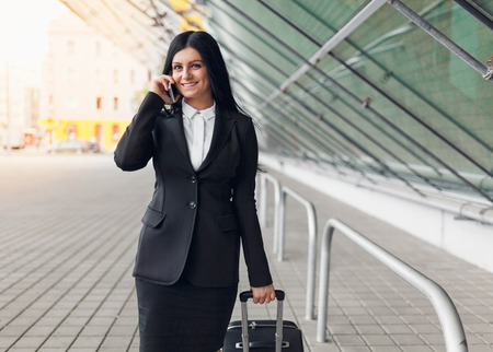Young beautiful business woman with mobile phone and suitcase in urban settingの写真素材