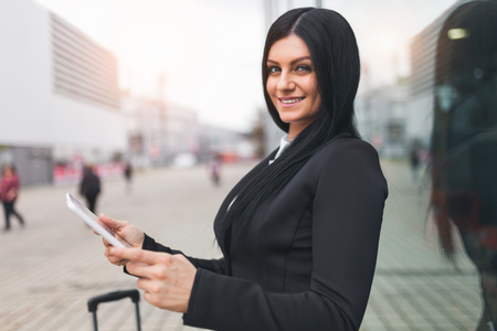 Young beautiful business woman with tablet and suitcase in an urban settingの写真素材