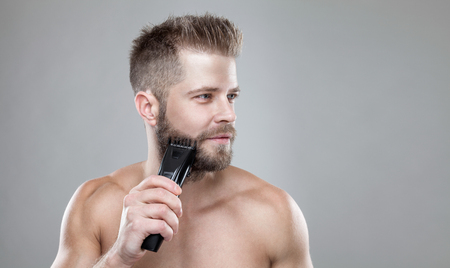 Handsome young bearded man trimming his beard with a trimmerの写真素材