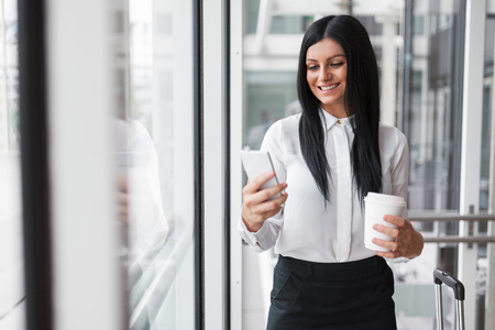 Successful confident young business woman with coffee and smartphone in an office settingの写真素材