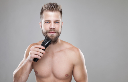 Handsome young bearded man trimming his beard with a trimmerの写真素材