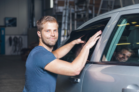 Applying tinting foil onto a car window in a workshopの写真素材