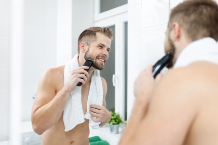 Handsome young bearded man trimming his beard with a trimmerの写真素材