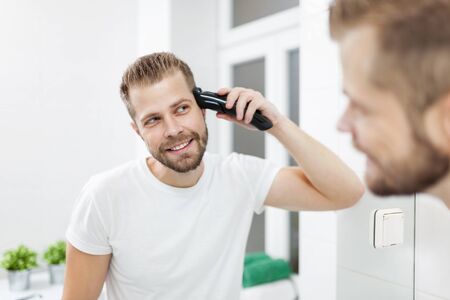 Handsome bearded man cutting his own hair with a clipperの写真素材
