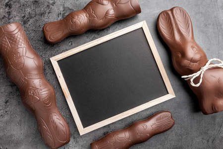 Traditional chocolate Easter bunnies and empty blackboard on rustic backgroundの写真素材