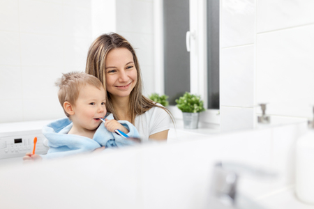 Happy mother teaching her son how to bush teeth in the bathroomの写真素材