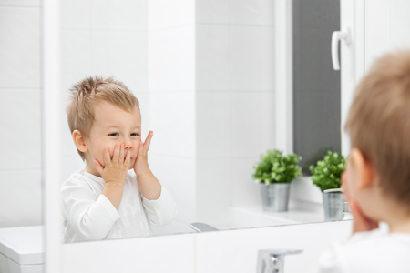 Cute toddler in the bathroom mirror learning how to wash his faceの写真素材