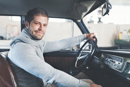 Handsome man sitting inside his old vintage carの写真素材