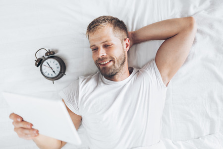 Handsome man using a digital tablet in bed at homeの写真素材