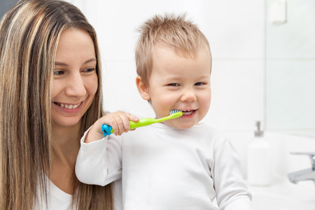 Happy mother teaching her son how to bush teeth in the bathroomの写真素材
