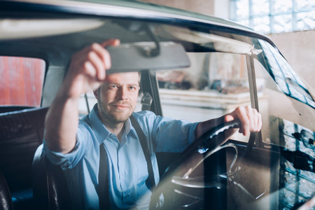 Handsome man sitting inside his old vintage carの写真素材