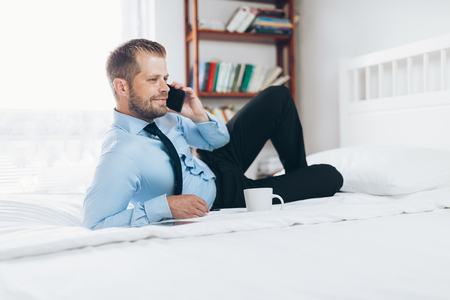 Young businessman working from a hotel room with his mobile phoneの写真素材
