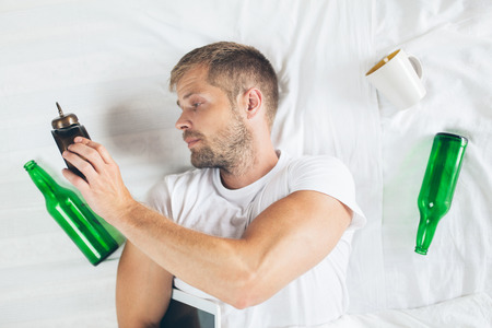 Young handsome man in bed the morning after night out drinkingの写真素材