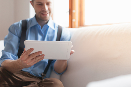 Handsome man sitting on sofa at home, using a digital tabletの写真素材