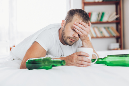 Young handsome man in bed the morning after night out drinkingの写真素材