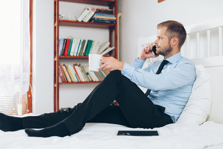 Young businessman working from a hotel room with his mobile phoneの写真素材