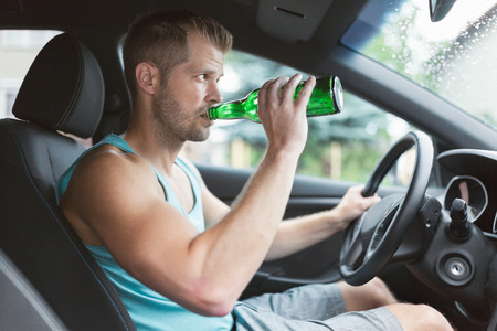 Drunk driver drinking behind the steering wheel of a carの写真素材