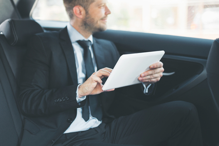 Executive businessman sitting at the back of car using a digital tabletの写真素材