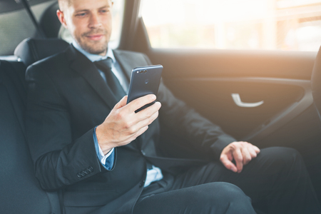 Executive businessman sitting at the back of car using a mobile phoneの写真素材