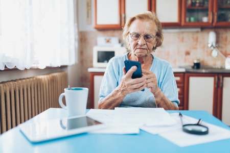 Elderly woman at home contacting custumer services after recieving a billの写真素材