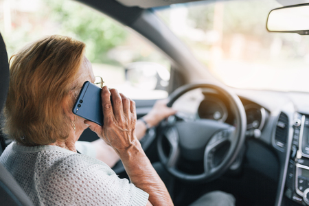 Elderly woman behind the steering wheel of a car using her phoneの写真素材
