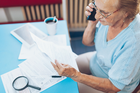 Elderly woman at home contacting custumer services after recieving a billの写真素材