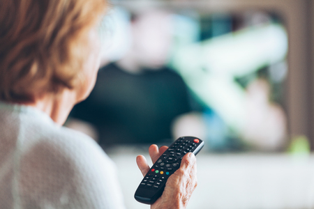 Senior woman with remote control watching televisionの写真素材