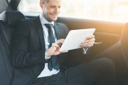 Executive businessman sitting at the back of car using a digital tabletの写真素材