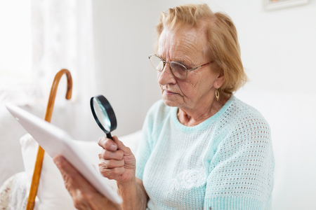 Elderly woman with glasses and loupe using a modern digital tabletの写真素材