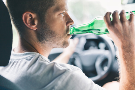 Drunk driver drinking behind the steering wheel of a carの写真素材