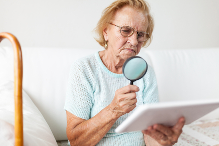 Elderly woman with glasses and loupe using a modern digital tabletの写真素材