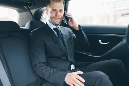 Executive businessman sitting at the back of car using a mobile phoneの写真素材