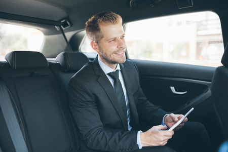 Executive businessman sitting at the back of car using a digital tabletの写真素材