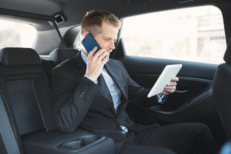 Executive businessman sitting at the back of car using a mobile phoneの写真素材