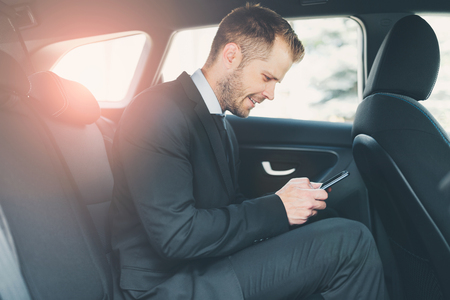 Executive businessman sitting at the back of car using a mobile phoneの写真素材