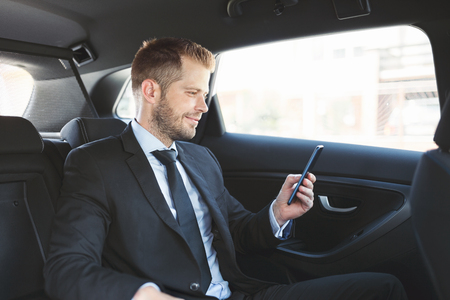Executive businessman sitting at the back of car using a mobile phoneの写真素材