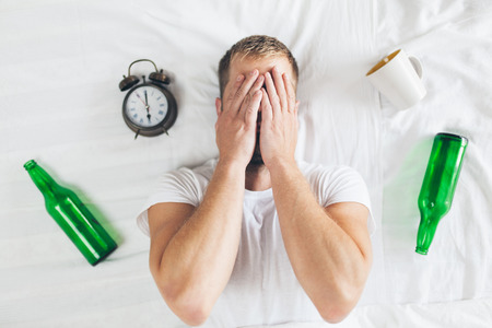Young handsome man in bed the morning after night out drinkingの写真素材