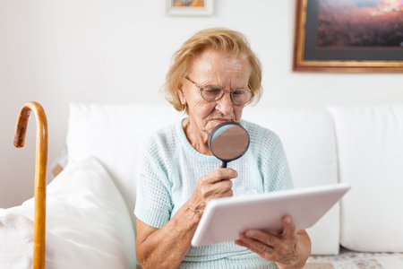 Elderly woman with glasses and loupe using a modern digital tabletの写真素材