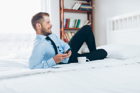 Young businessman working from a hotel room with his mobile phoneの写真素材