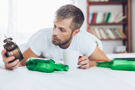Young handsome man in bed the morning after night out drinkingの写真素材