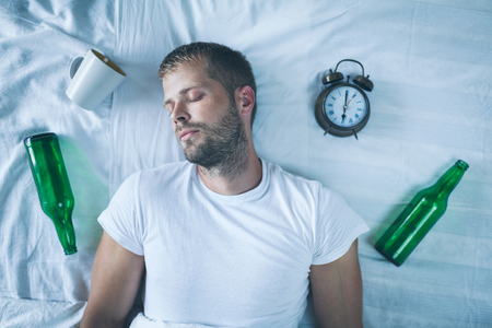 Young handsome man in bed the morning after night out drinkingの写真素材